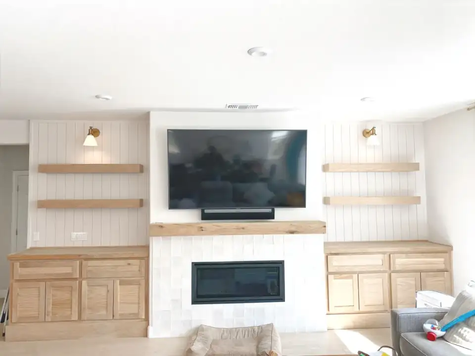 Living room wall with a central fireplace and television flanked by wood cabinets and open shelves