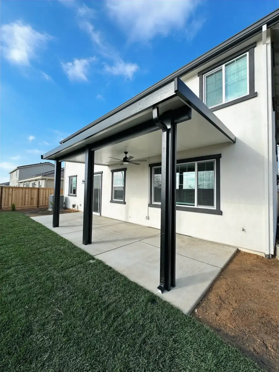 Modern black-post patio cover attached to a two-story home above a concrete patio