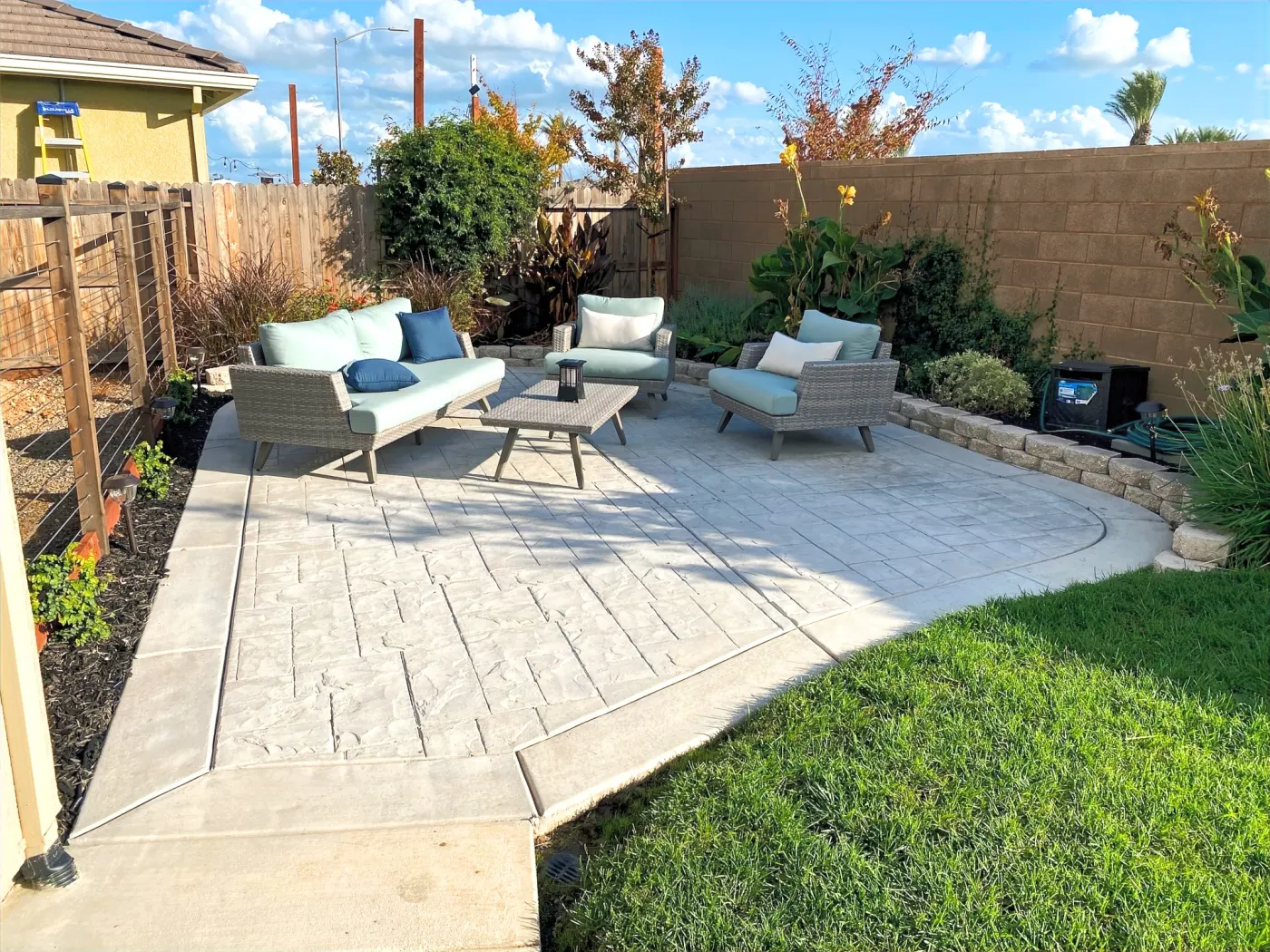 Stamped concrete backyard patio with outdoor chairs beside a green lawn and planted border